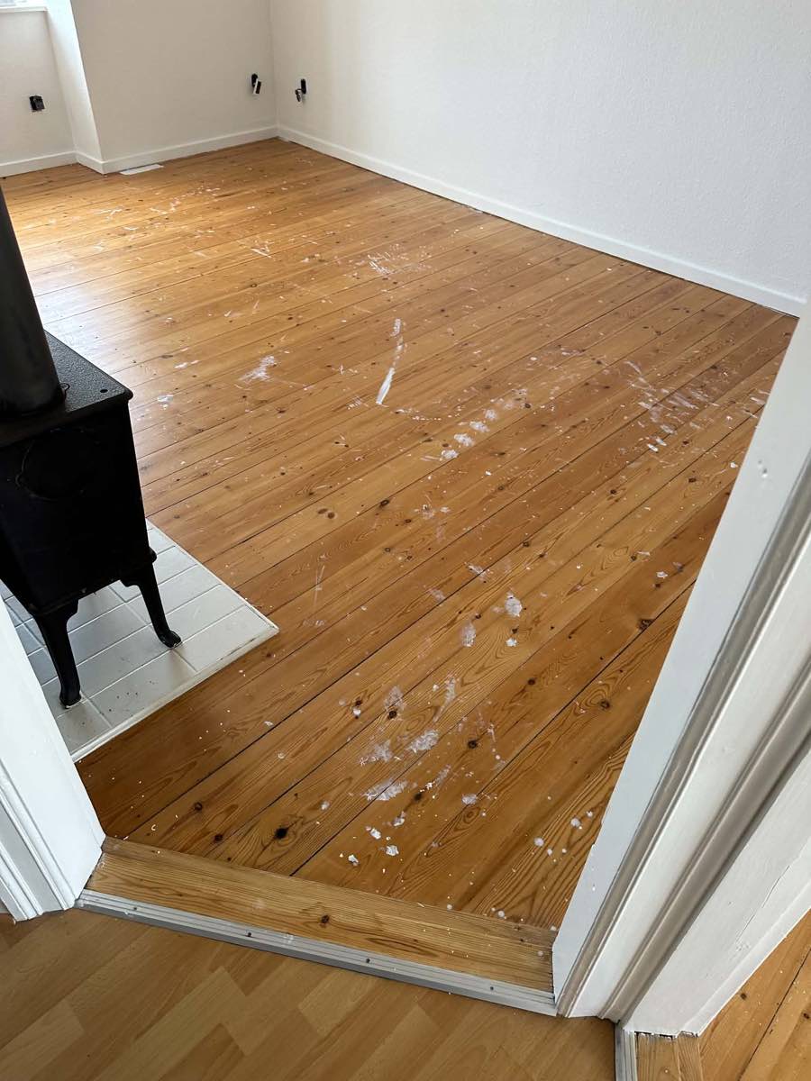 Før: plankegulv med malingspletter ved brændeovn